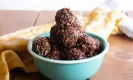 chocolate coconut macaroons in a turquoise bowl on a wooden surface, with a yellow napkin behind.