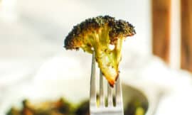A perfectly crispy piece of air fryer broccoli held up on a fork.