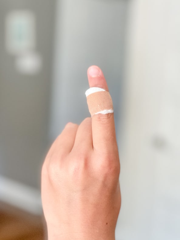 A vertical shot of a close up of a hand with one finger up, with a DIY wart bandaid on it.