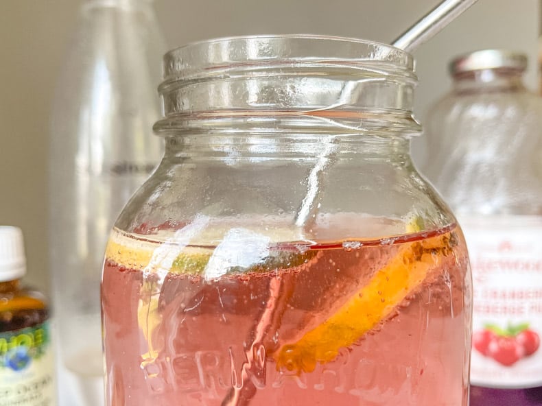 A mason jar of fizzy rose coloured Red and Honey Detox drink with a reusable metal straw.