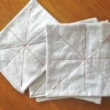 overhead shot of cloth baby wipes on a wooden surface. wipes are white fabric squares with red thread sewn in a starburst pattern.